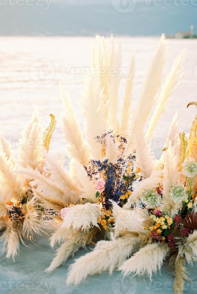 kleurrijk bruiloft semi-boog gemaakt van droog bloemen staat Aan een pier door de zee foto