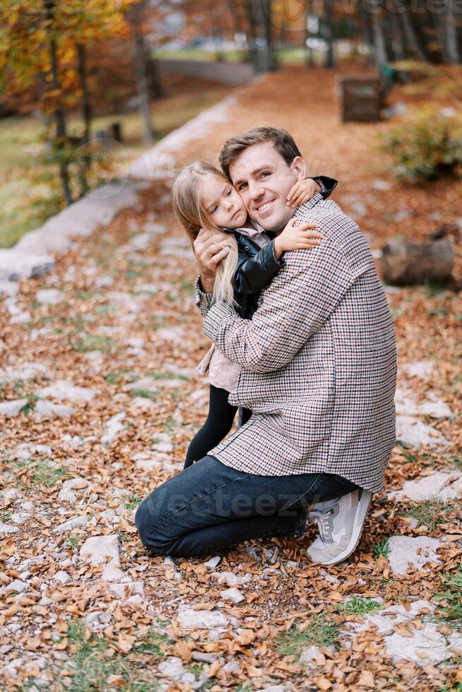 glimlachen vader knuffelen weinig dochter terwijl geknield in herfst park foto