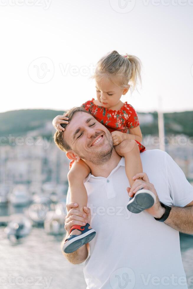 weinig meisje onderzoekt haar vader gezicht terwijl zittend Aan zijn schouders en Holding zijn hoofd foto