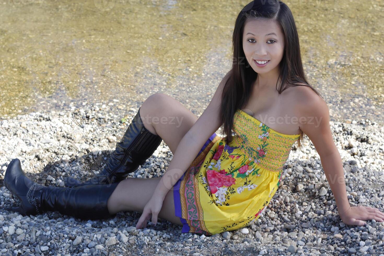 Aziatisch Amerikaans vrouw in geel jurk en zwart laarzen Bij rivier- foto