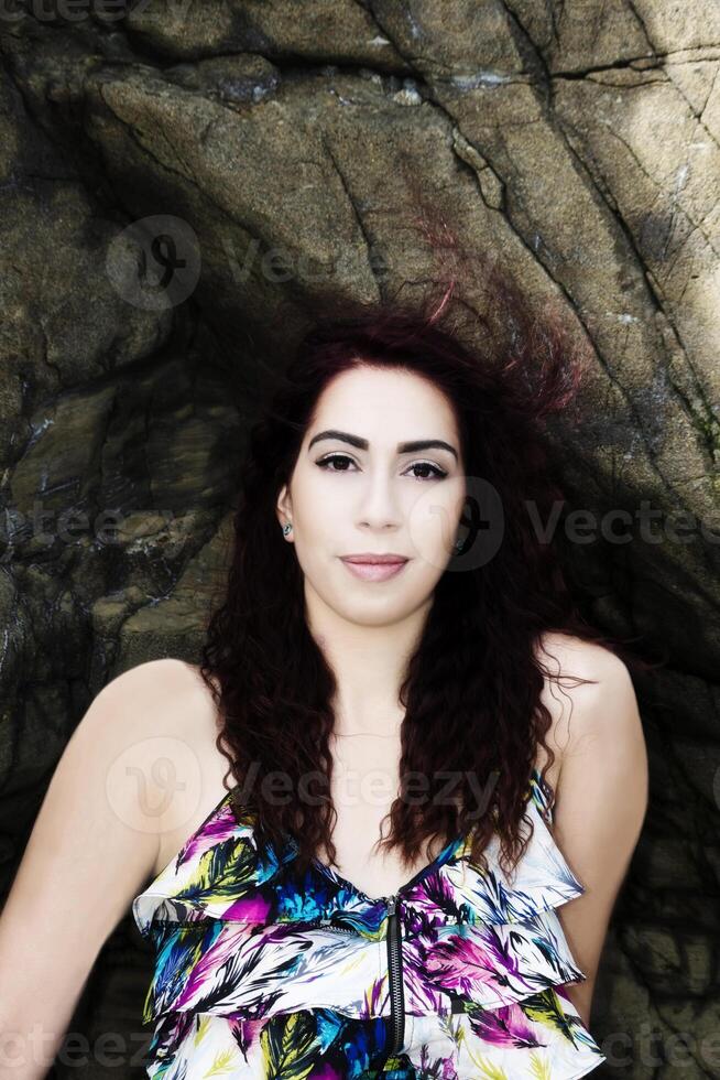 latina vrouw zittend Aan rotsen portret in jurk foto