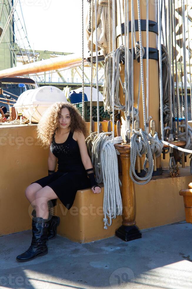 gemengd ras aantrekkelijk jong vrouw zittend Aan het zeilen schip foto