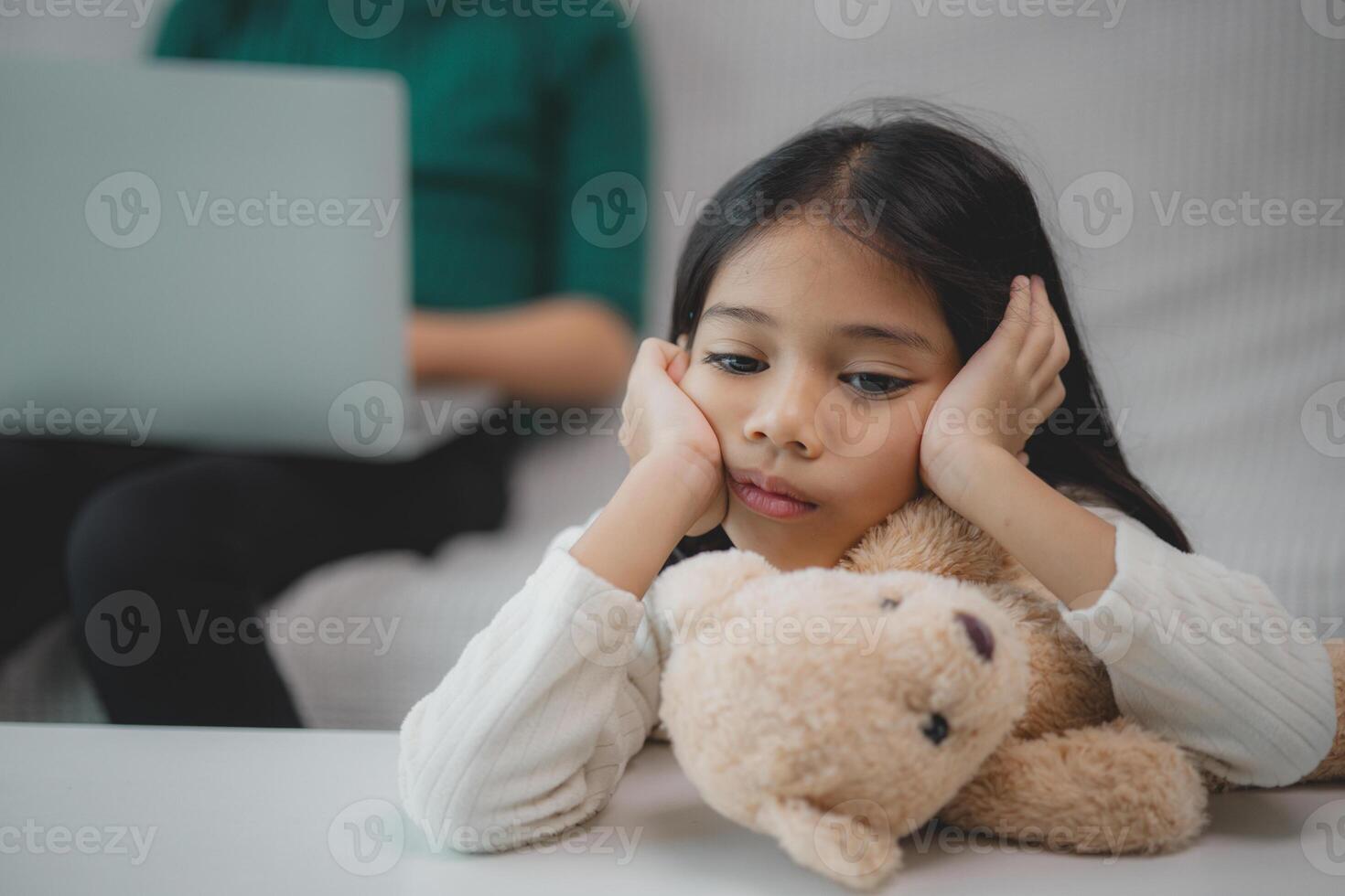 een jong meisje is zittend Aan een bankstel met een teddy beer in haar ronde foto