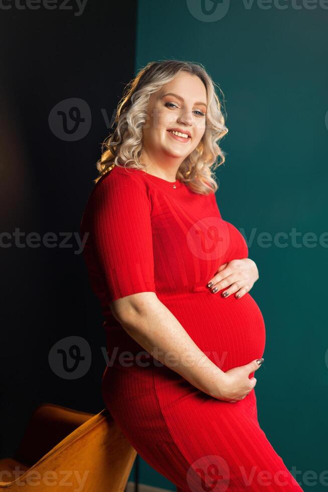 zwanger vrouw poseren in een elegantrood jurk binnenshuis studio zwart muur achtergrond foto