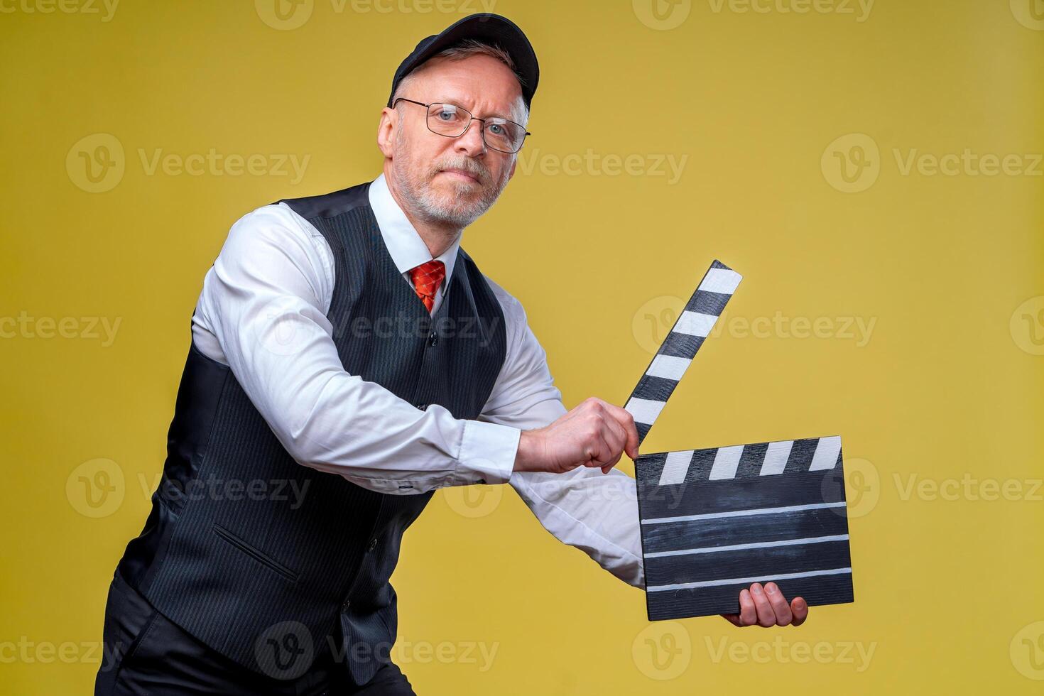 senior glimlachen regisseur met film klep. geel achtergrond. filmen. film regisseren. film productie. menselijk emoties. foto