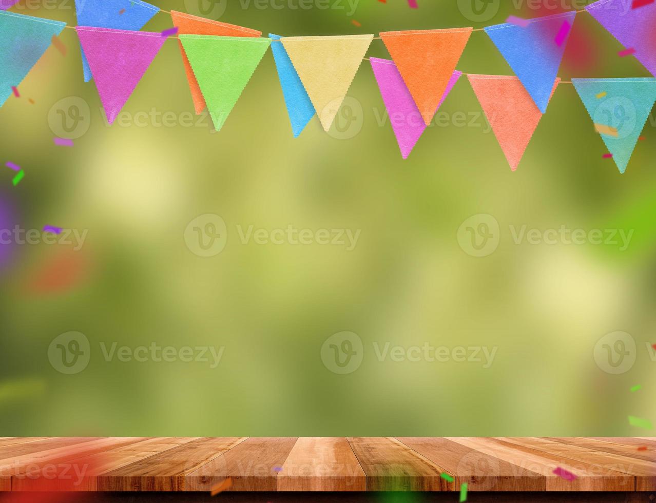 kleurrijke vlag banner en confetti op houten tafel met groene boom bokeh achtergrond wazig. foto