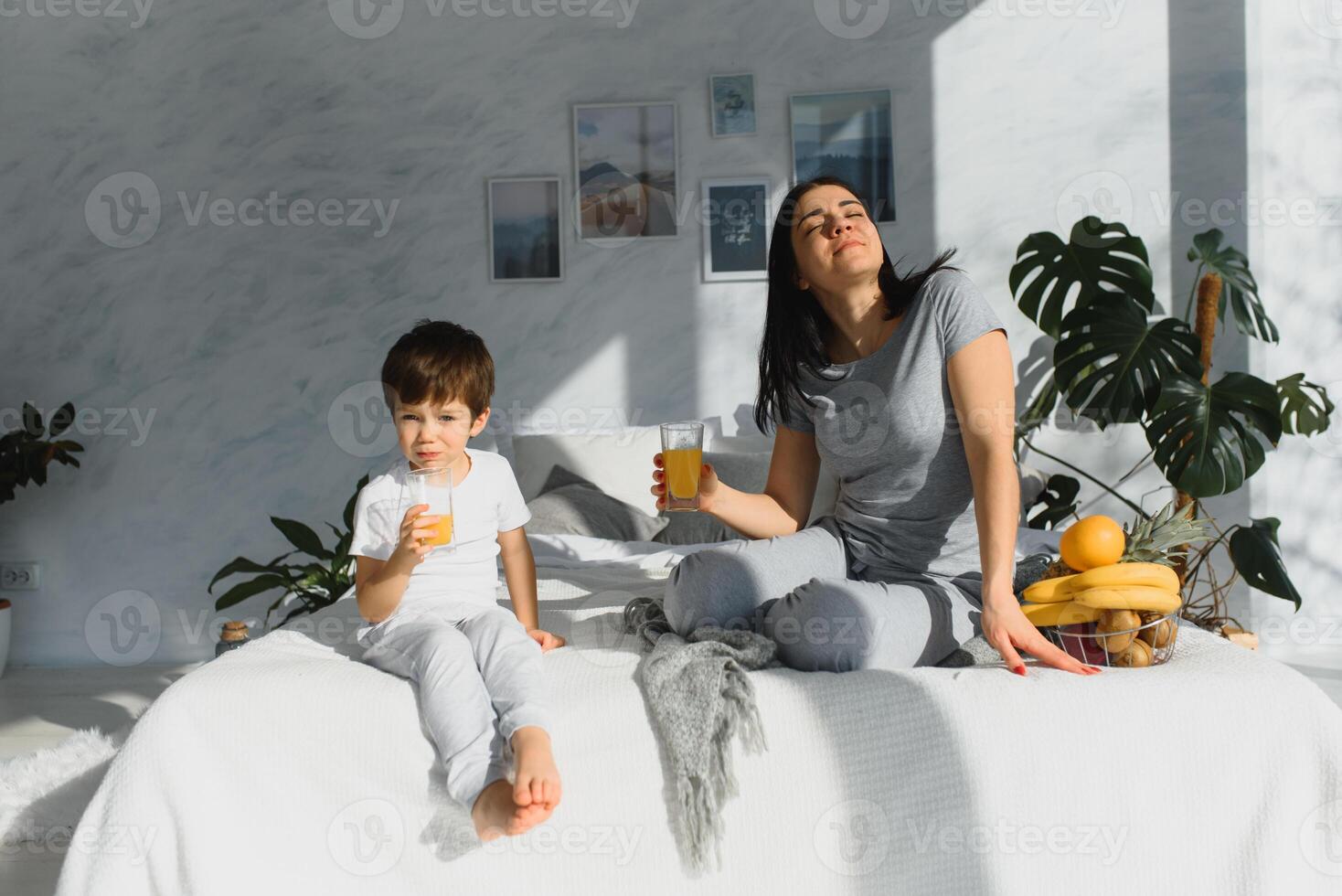 mam met zoon in pyjama aan het eten fruit Aan bed. portret Vrolijk, lachend, blij familie, moeder en zoon hebben ontbijt in bed, verrassing Aan mam dag. positief menselijk emoties foto
