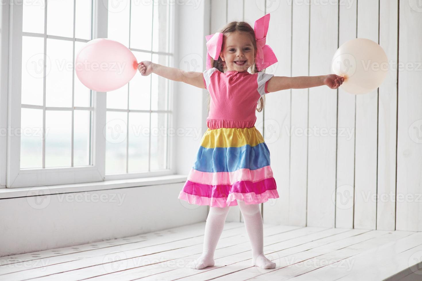 ballonnen uit. kind staat naast de ramen in de witte kamer en poseert voor de foto