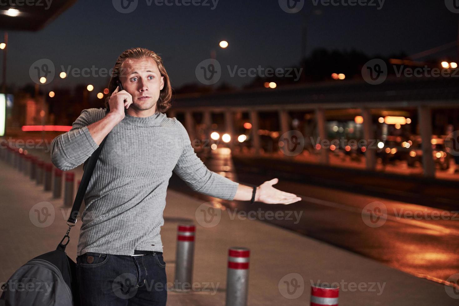jonge stylih man die door de nachtelijke boom in de buurt van de weg loopt en een gesprek voert aan de telefoon foto