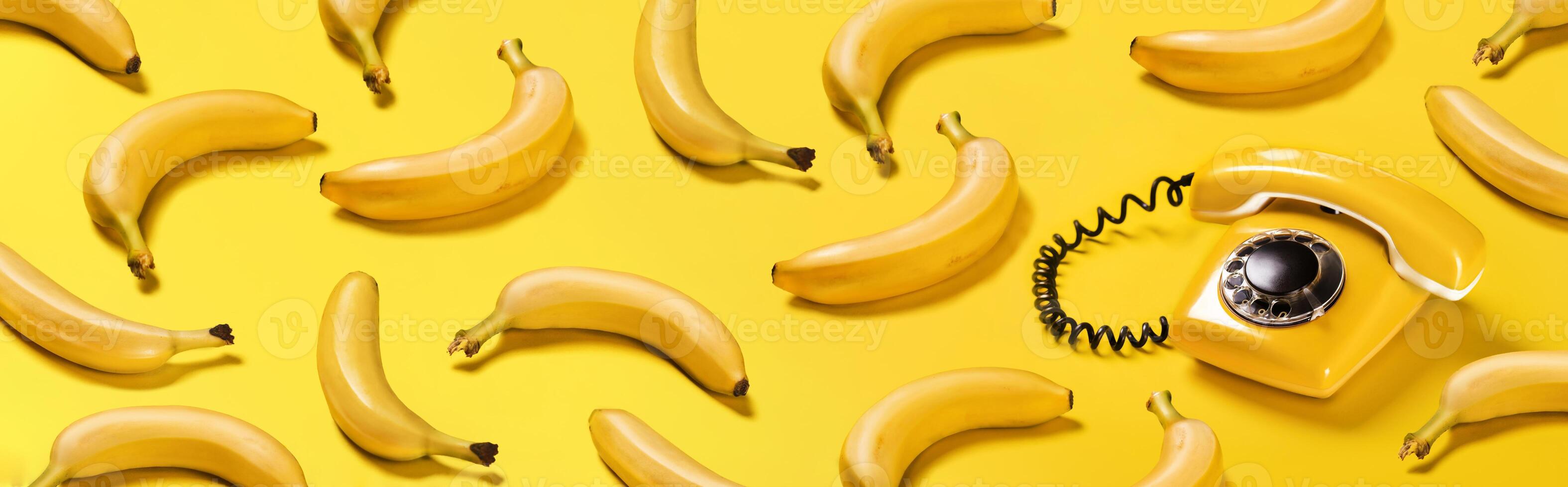 banier bananen en oud geel telefoon met moeilijk schaduwen patroon Aan geel achtergrond bananentelefoon foto
