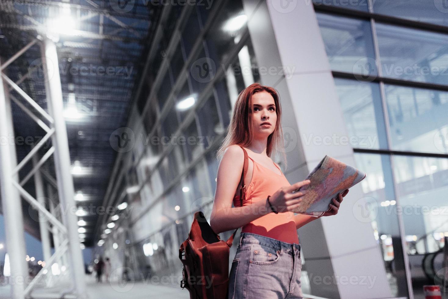 ver weg kijken. aantrekkelijk meisje dat in de buurt van de luchthaven loopt en naar de kaart in haar handen kijkt foto