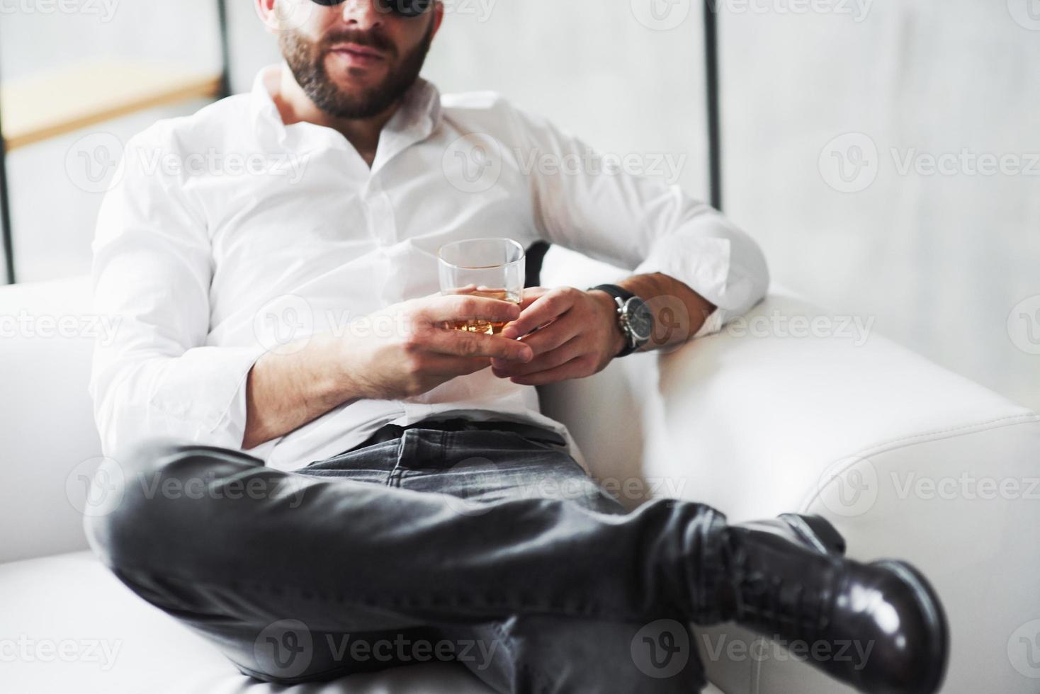 vooraanzicht. bijgesneden foto van een jonge zakenman in klassieke kleding zittend op de bank met whiskyglas in de hand