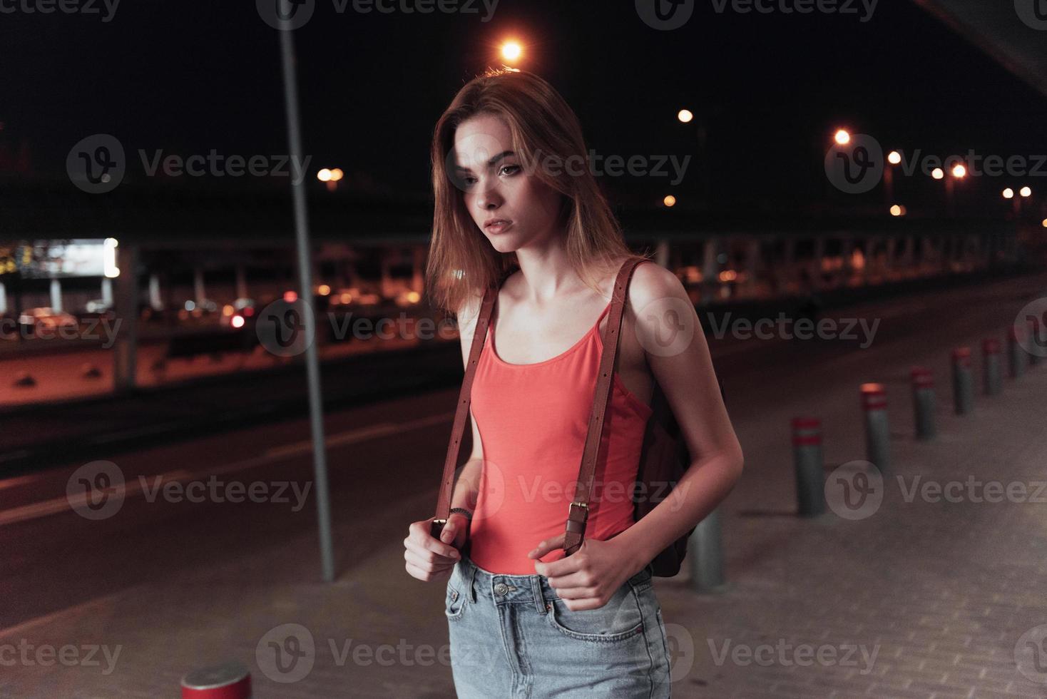 reizende jonge vrouw die haar tas vasthoudt terwijl ze in de buurt van de weg staat en wacht op het transport foto