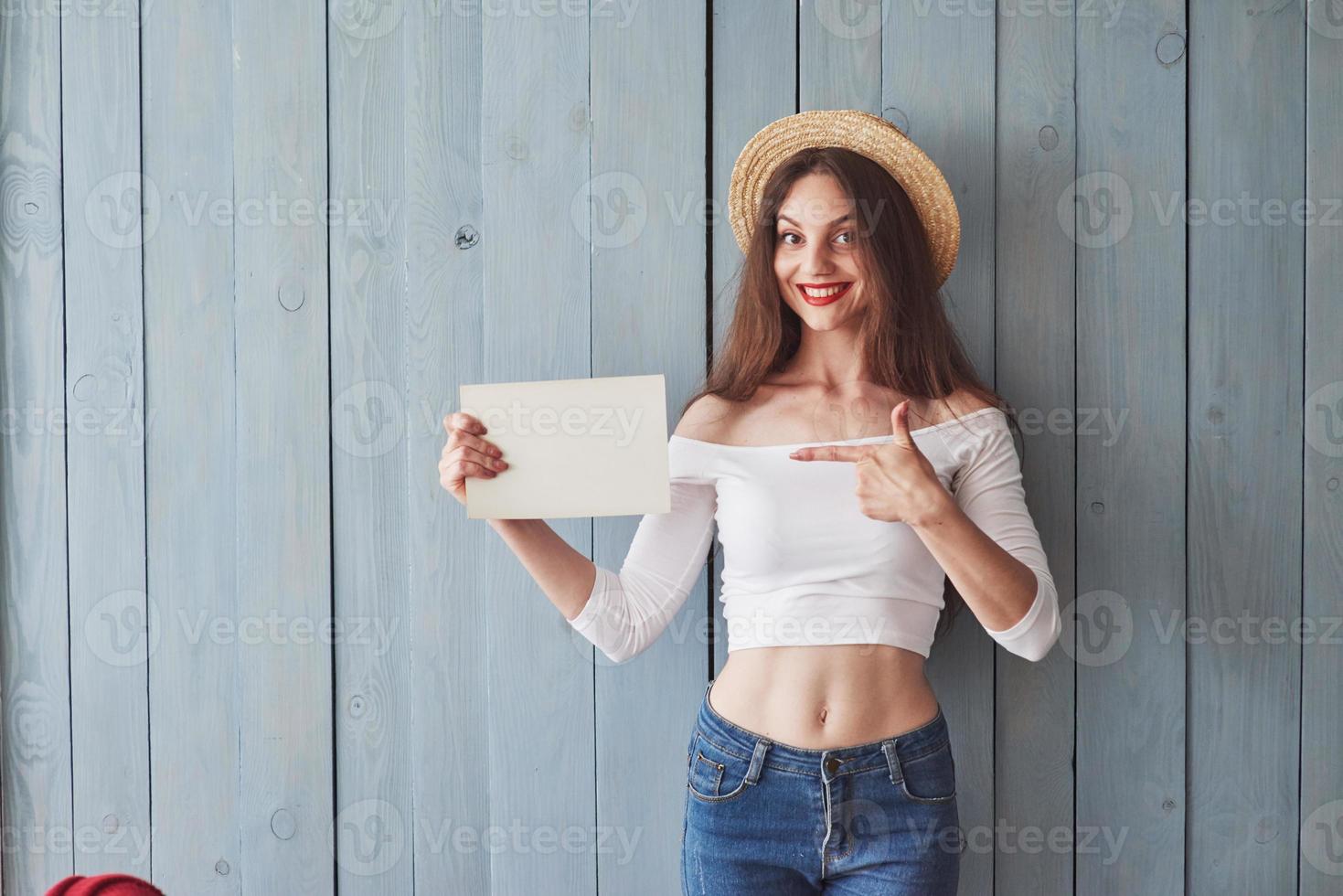 leeg papier in de rechterhand en wijsvinger. jonge vrouw die binnen staat en glimlacht foto