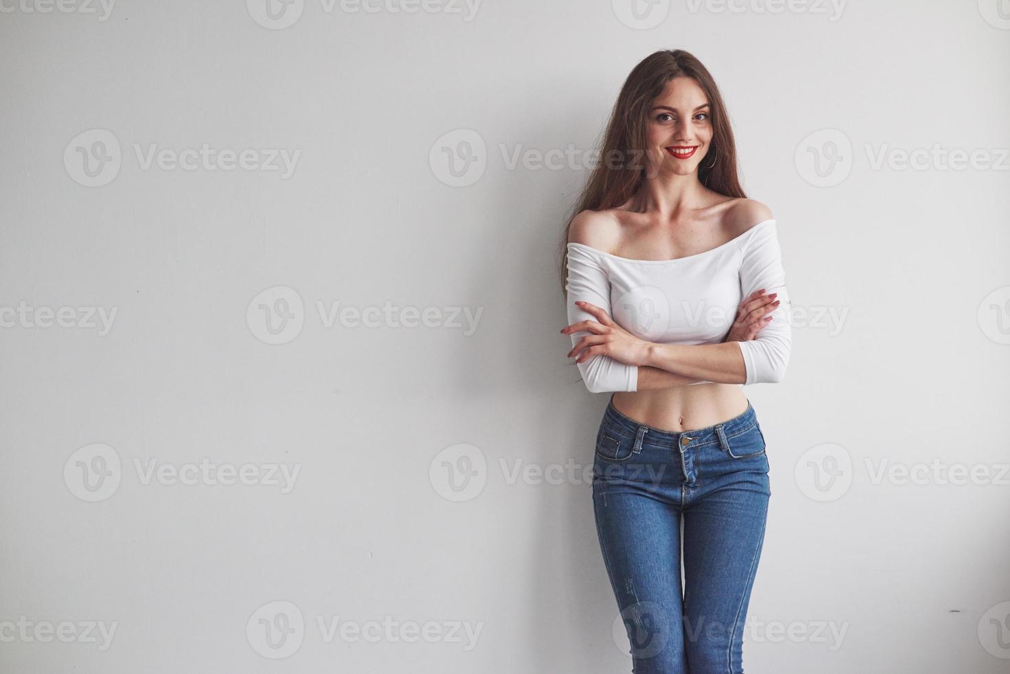 prachtige glimlachende jonge vrouw die met gekruiste handen tegen de muur staat foto