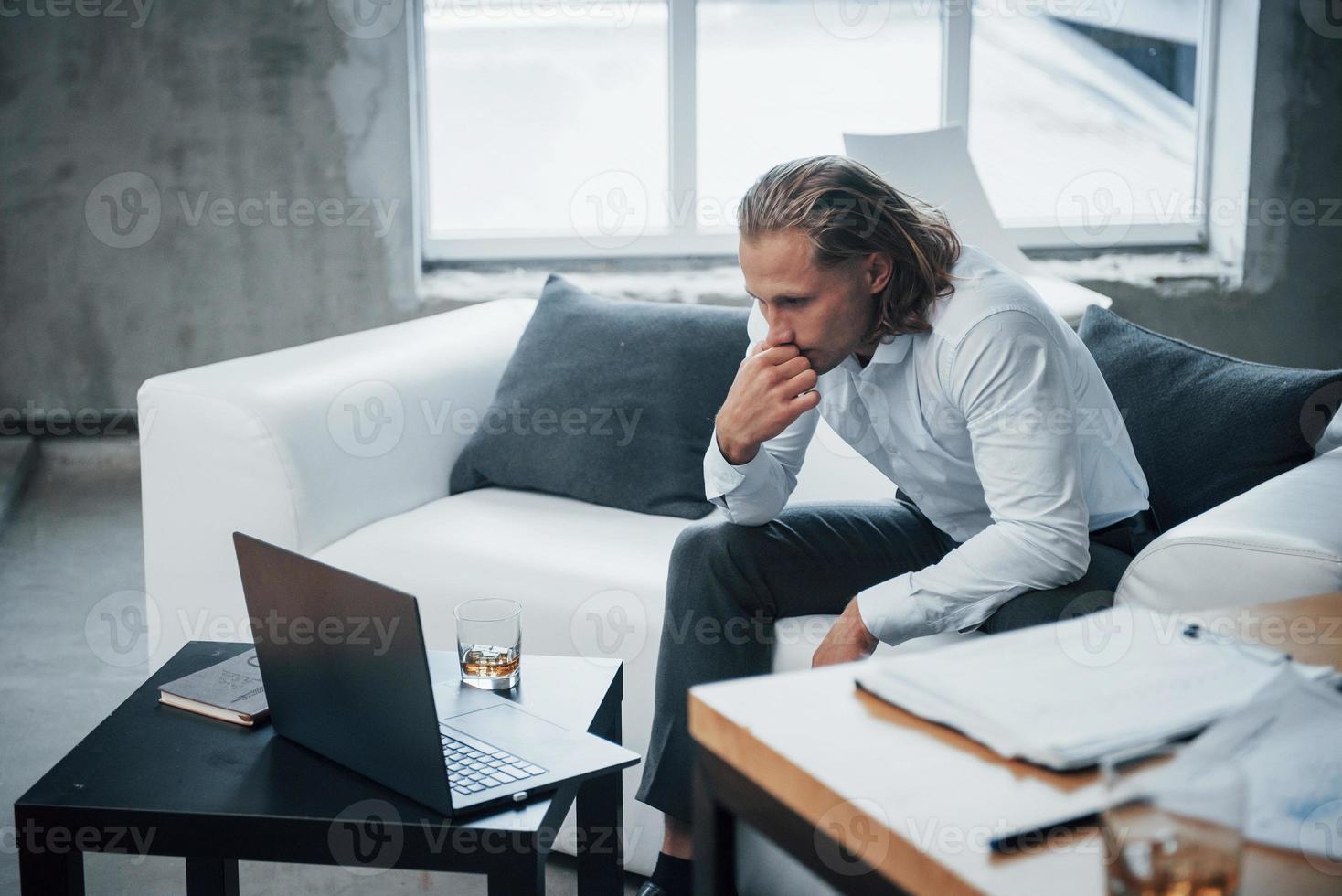 overwerkte jonge zakenman zittend op de bank en kijken op laptop foto