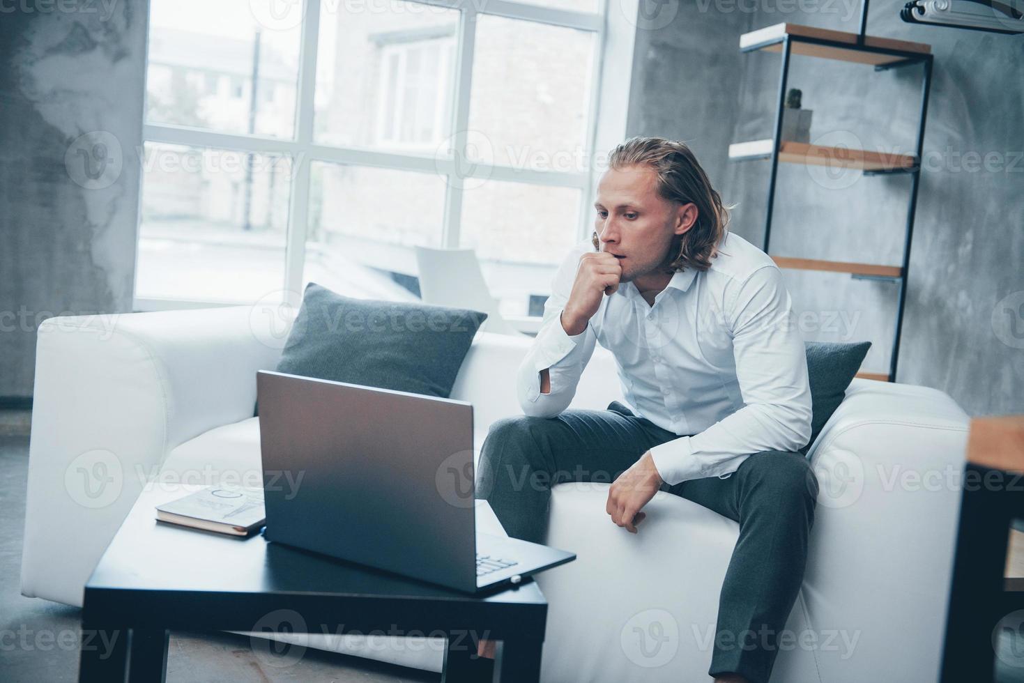 bezorgd en vermoeide blik. overwerkte jonge zakenman zittend op de bank en kijken op laptop foto