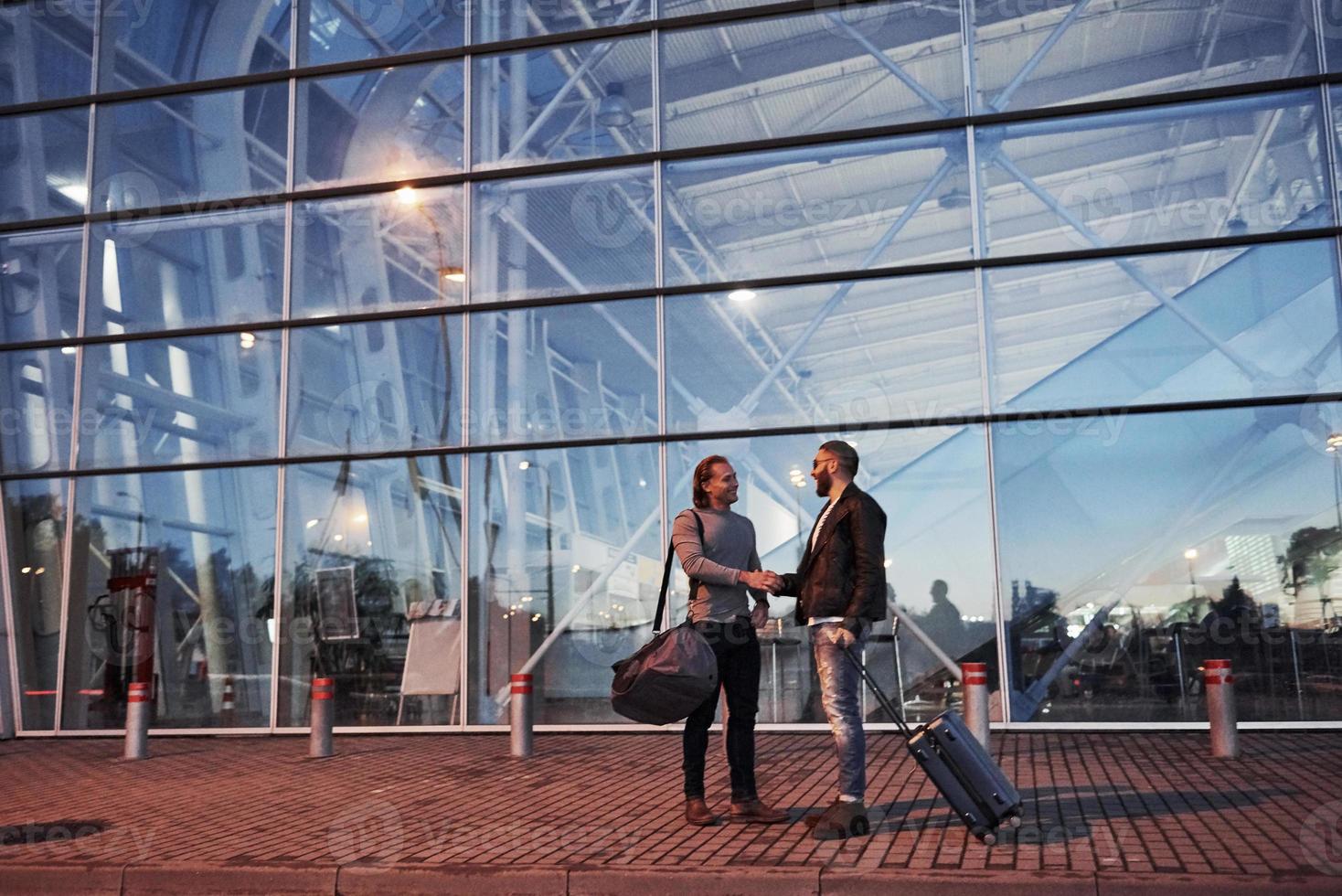 twee stijlvolle vrienden met bagage hebben elkaar ontmoet in de buurt van een zakencentrum foto