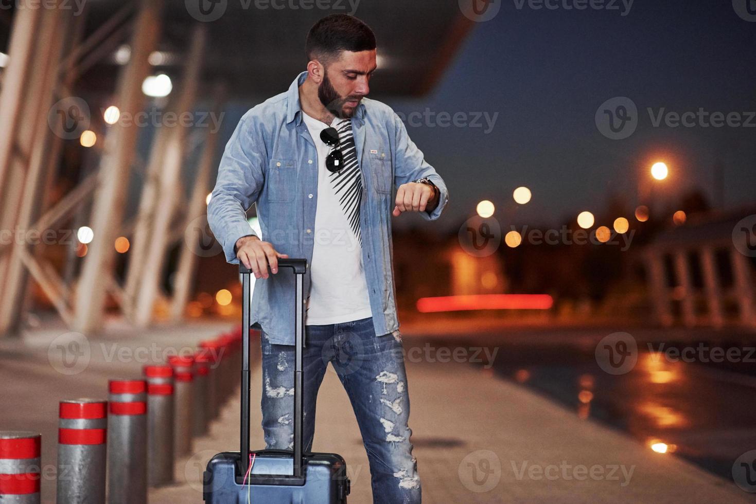 man met kort haar en reisbagage die wacht op de taxi om hem op te halen foto