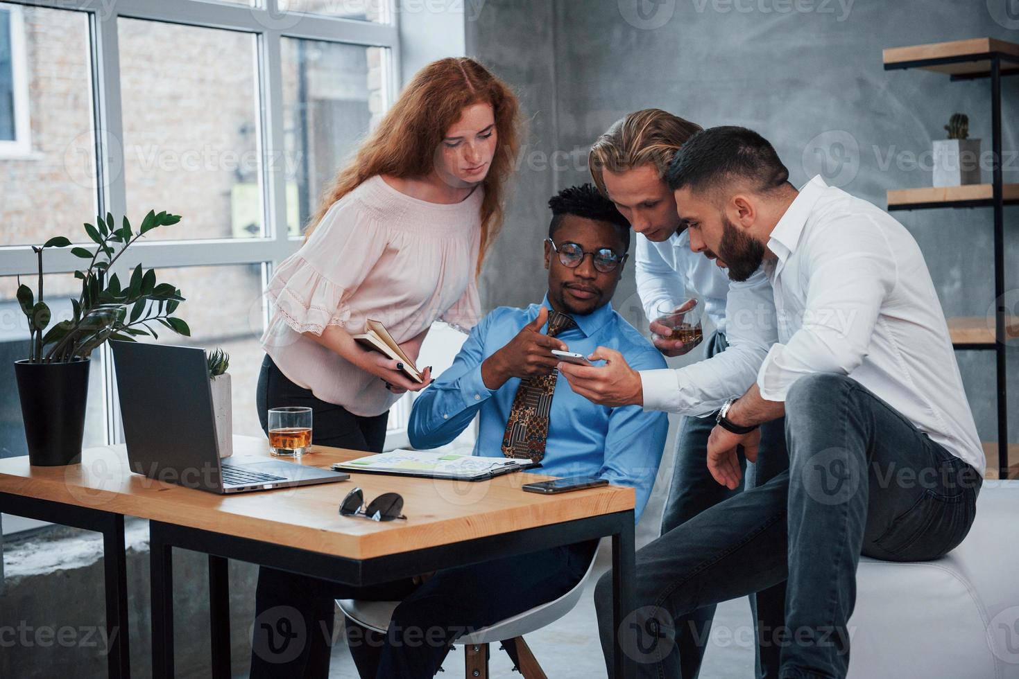 smartphone gebruiken om informatie te vinden. groep multiraciale kantoormedewerkers in formele kleding praten over taken en plannen foto