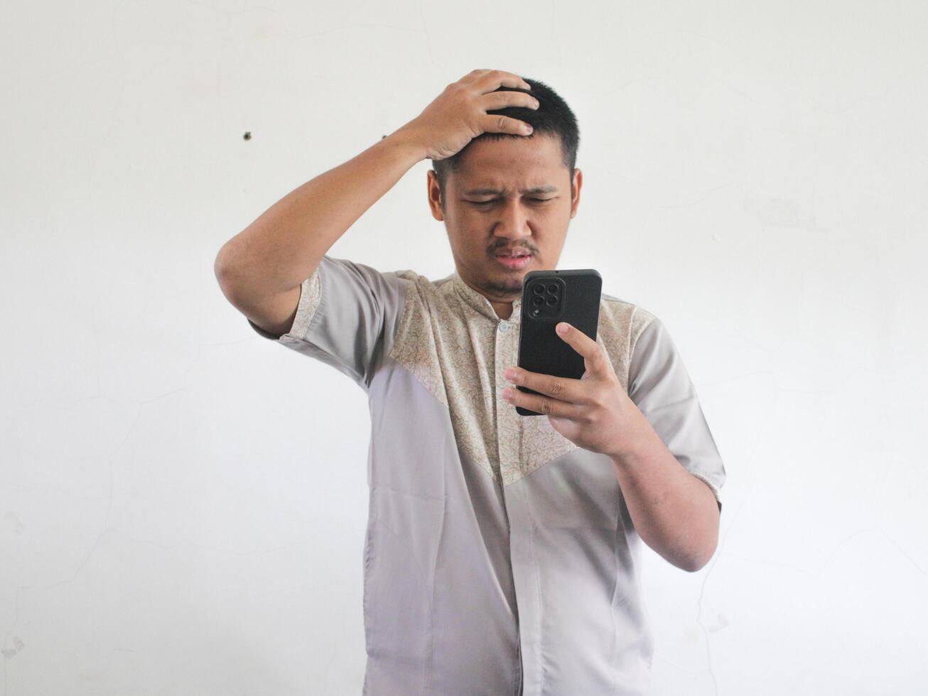 volwassen Aziatisch Mens tonen verward uitdrukking wanneer op zoek naar zijn telefoon foto