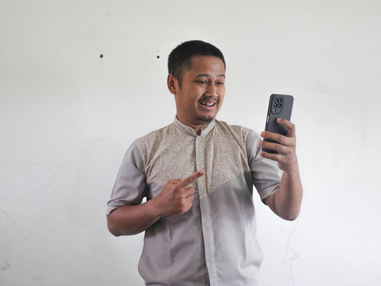 volwassen Aziatisch Mens op zoek en richten naar zijn handtelefoon met versteld staan uitdrukking foto