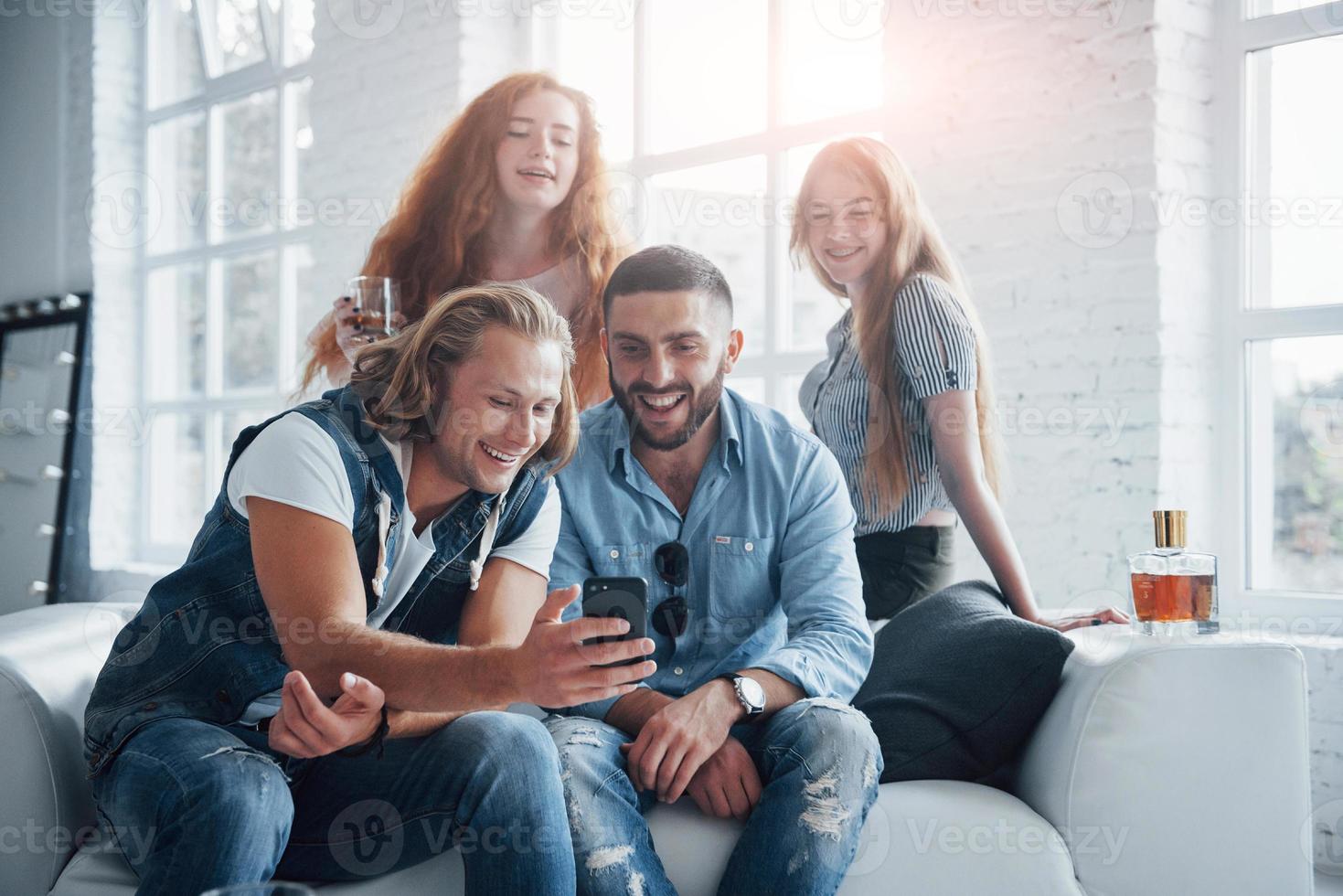 groep vrienden kijken naar iets grappigs op de smartphone die wordt weergegeven door een blonde man foto