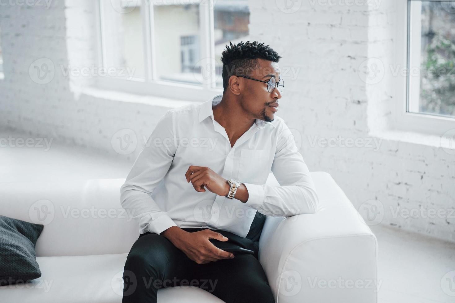 door het raam kijken wat er buiten gebeurt. stijlvolle afro-amerikaanse man in klassieke kleding en bril foto