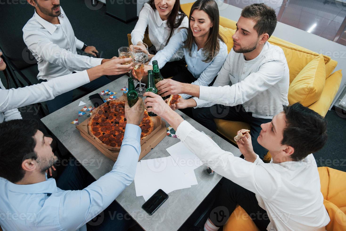 bovenaanzicht. succesvolle deal vieren. jonge kantoormedewerkers zitten bij de tafel met alcohol foto