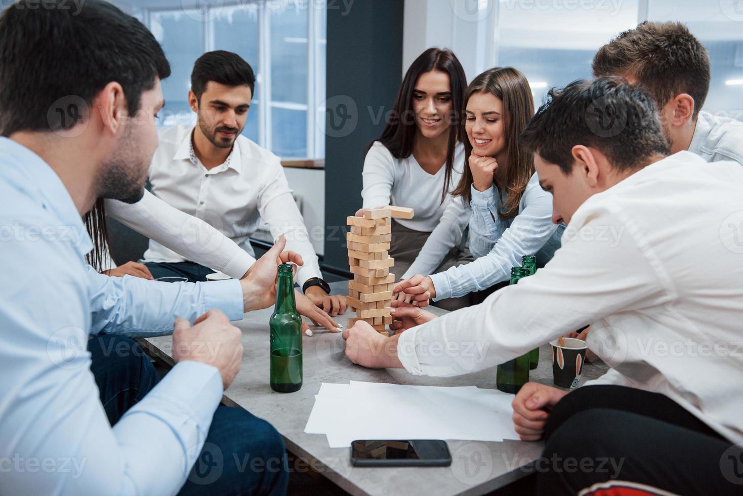 moet voorzichtig zijn bij het spelen van dit spel. succesvolle deal vieren. jonge kantoormedewerkers zitten bij de tafel met alcohol foto