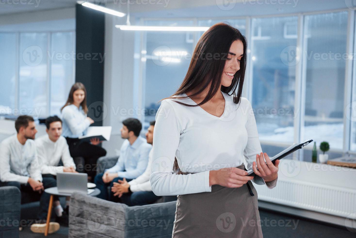 het lezen van het rapport. portret van een jong meisje staat op kantoor met medewerkers op de achtergrond foto