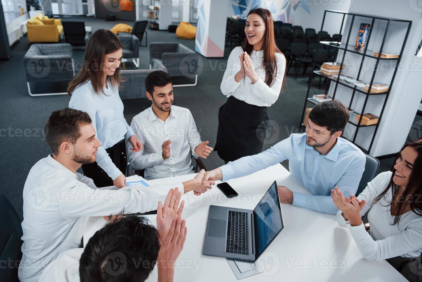 deal tussen bedrijven succesvol. bovenaanzicht van kantoormedewerkers in klassieke kleding die bij de tafel zitten met laptop en documenten foto