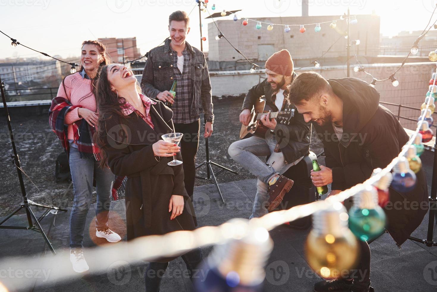 luid lachen. overal gloeilampen op het dak waar een jonge groep vrienden heeft besloten hun weekend door te brengen met gitaar en alcohol? foto