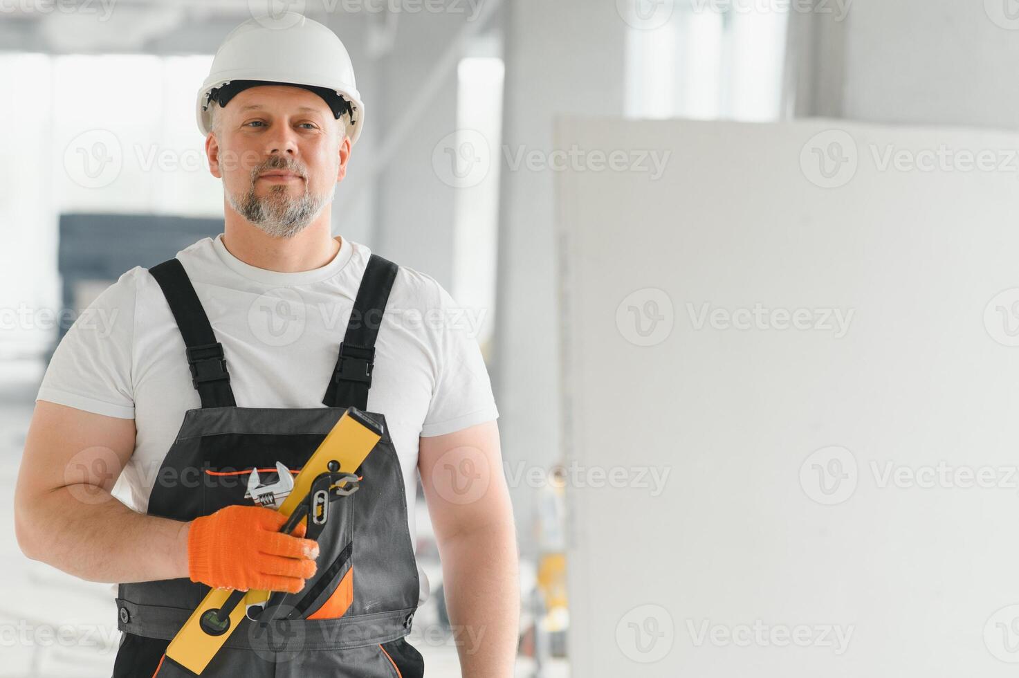 een Mens met een baard in een helm en werk kleren. portret van een arbeider in werkkleding met kopiëren ruimte. foto