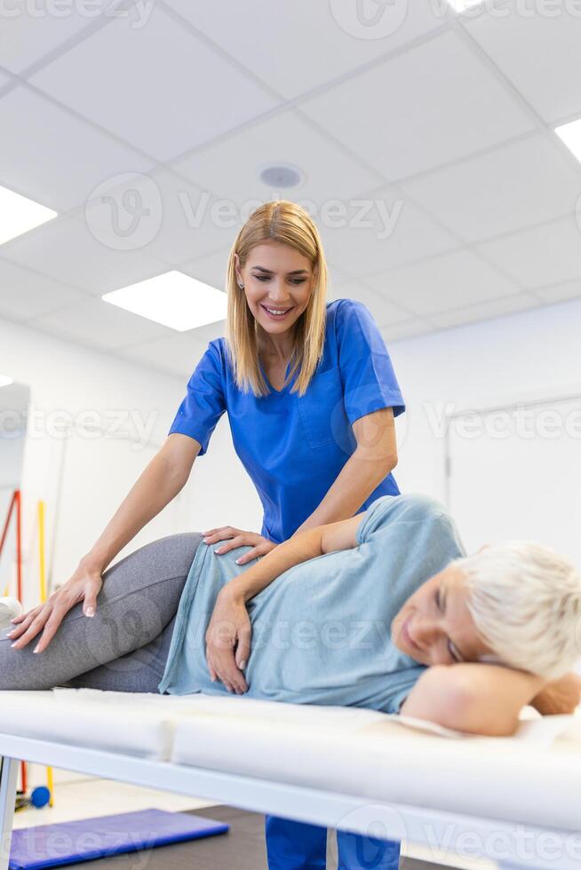 professioneel chiropractor of fysiotherapeut helpt naar genezen een senior vrouw rug. dokter reparaties de geduldig aan het liegen Aan een bankstel van een modern revalidatie kliniek concept van fysiek revalidatie. foto