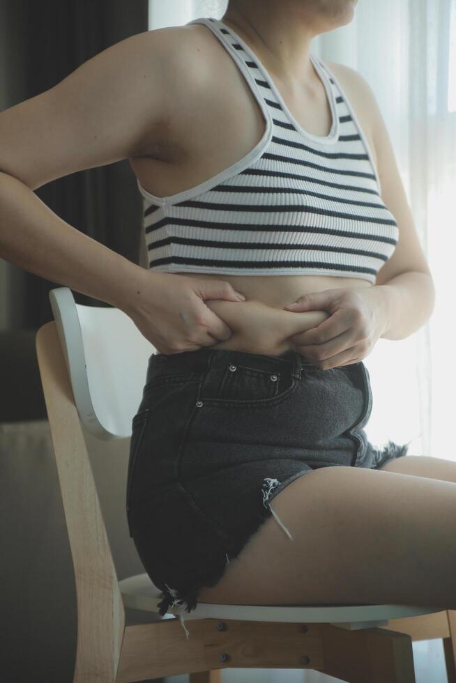 Dames lichaam dik buik. zwaarlijvig vrouw hand- Holding buitensporig buik dik. eetpatroon levensstijl concept naar verminderen buik en vorm omhoog gezond maag spier. foto