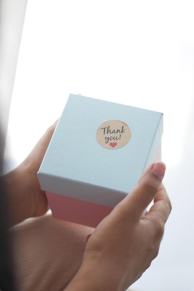 hand- zetten een dank u sticker Aan een geschenk doos foto