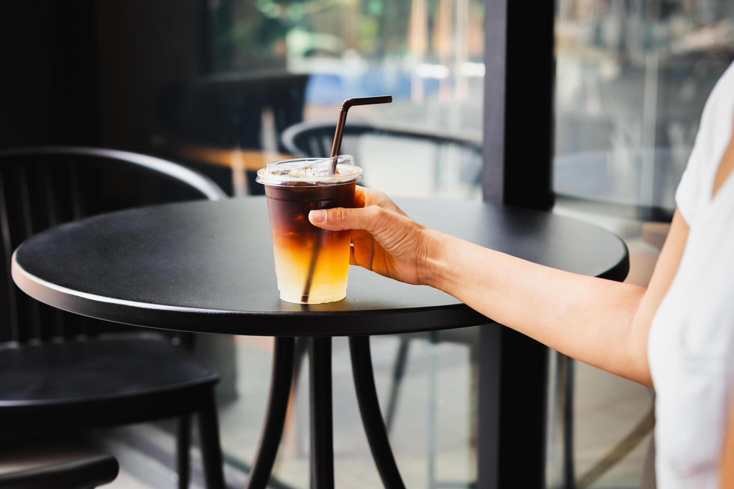 vrouw drinken bevroren koffie in meenemen plastic kop Bij tafel buitenshuis cafe. foto