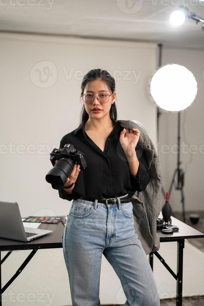 een zelfverzekerd Aziatisch vrouw fotograaf is staand in haar studio met een dslr camera in haar hand. foto