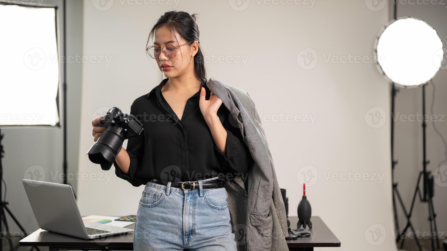 een zelfverzekerd Aziatisch vrouw fotograaf is staand in haar studio met een dslr camera in haar hand. foto