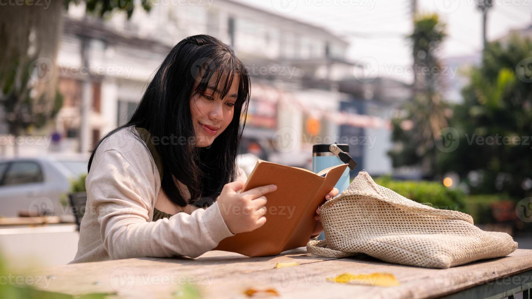 een aantrekkelijk, gelukkig Aziatisch vrouw is lezing een boek Bij een tafel buitenshuis in de stad. foto