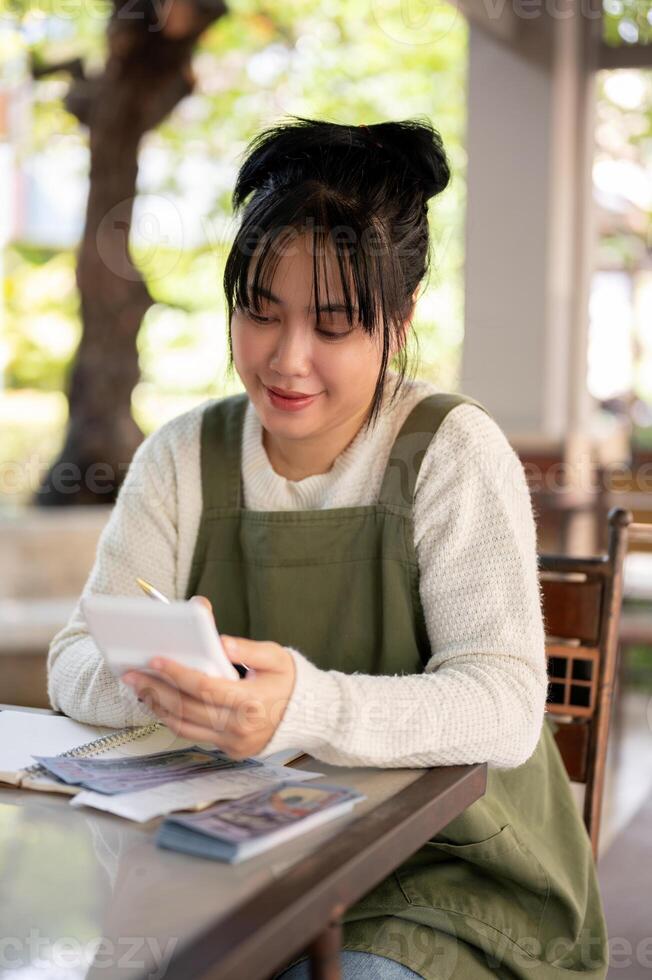 een positief Aziatisch vrouw klein bedrijf eigenaar gebruik makend van een rekenmachine, berekenen haar winkel omzet. foto