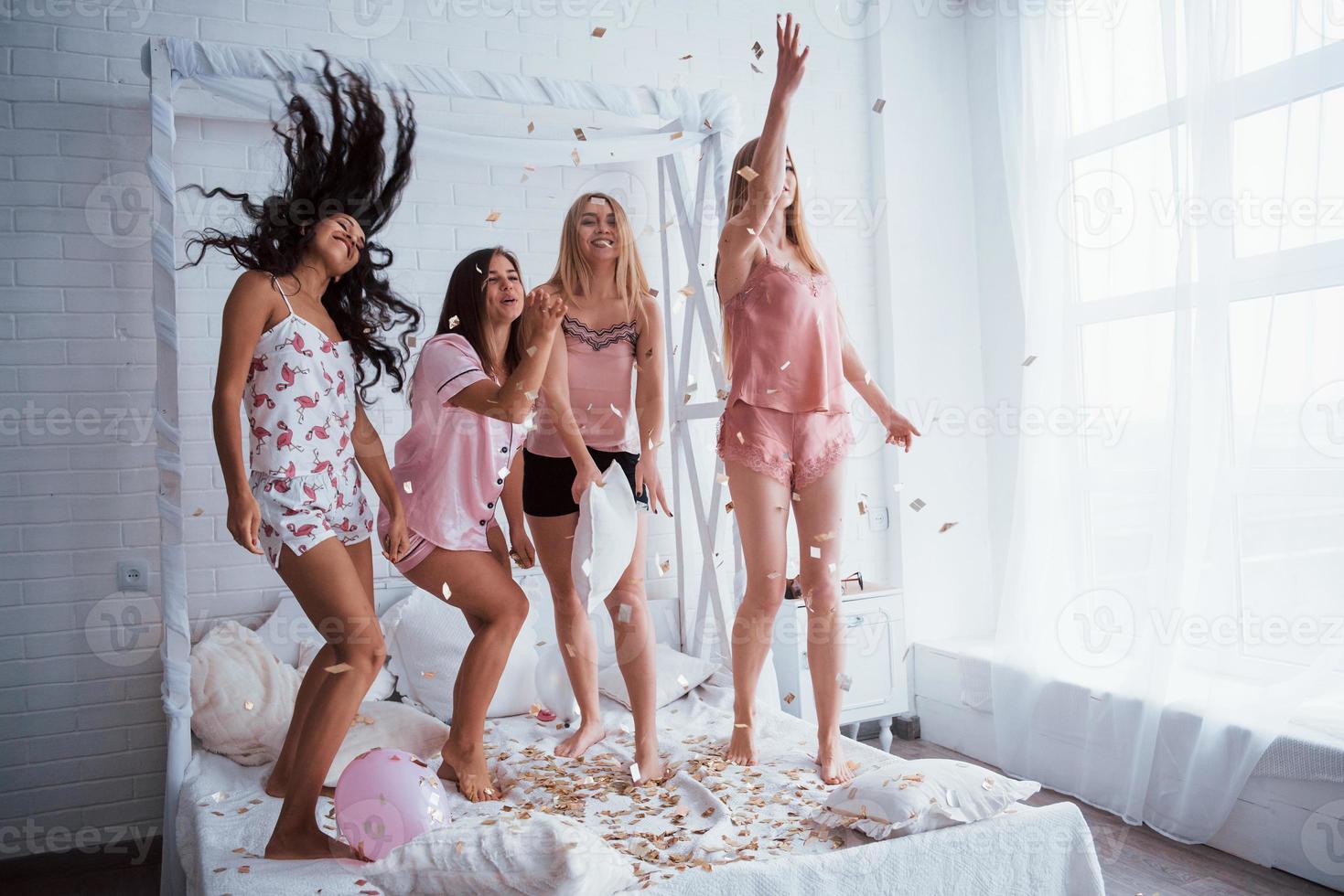 deze mensen weten hoe ze moeten feesten. confetti in de lucht. jonge meisjes hebben plezier op het witte bed in een mooie kamer foto