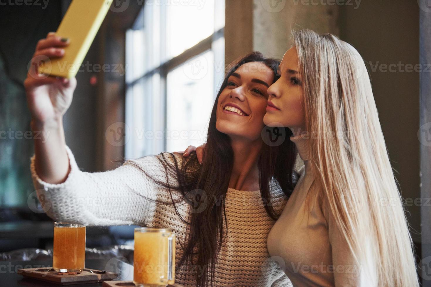 jonge vriendinnen nemen selfie in het restaurant met twee gele drankjes op tafel foto