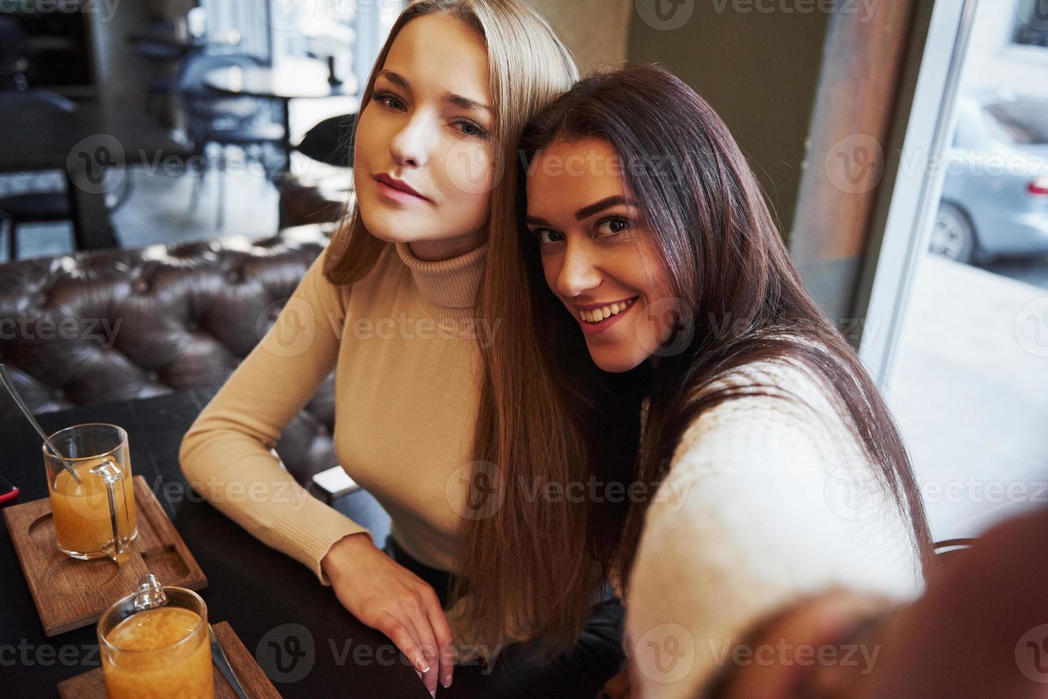 op de langgerekte hand. jonge vriendinnen nemen selfie in het restaurant met twee gele drankjes op tafel foto