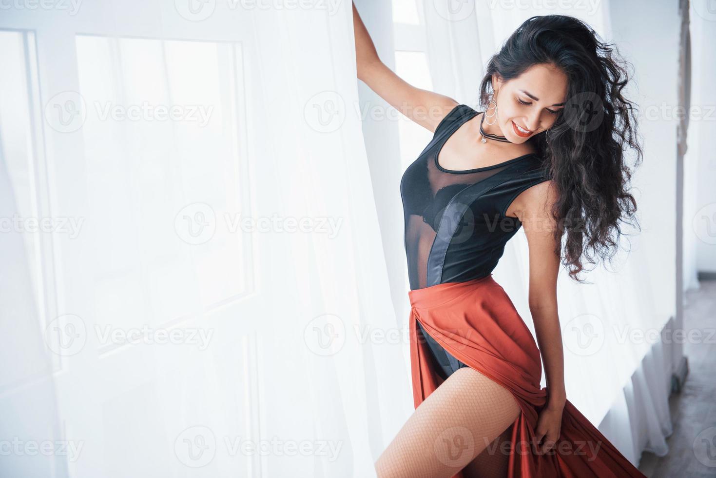 hand is op gordijnen. mooie danseres in de zwarte en rode kleren oefenen in de witte kamer bij het raam foto