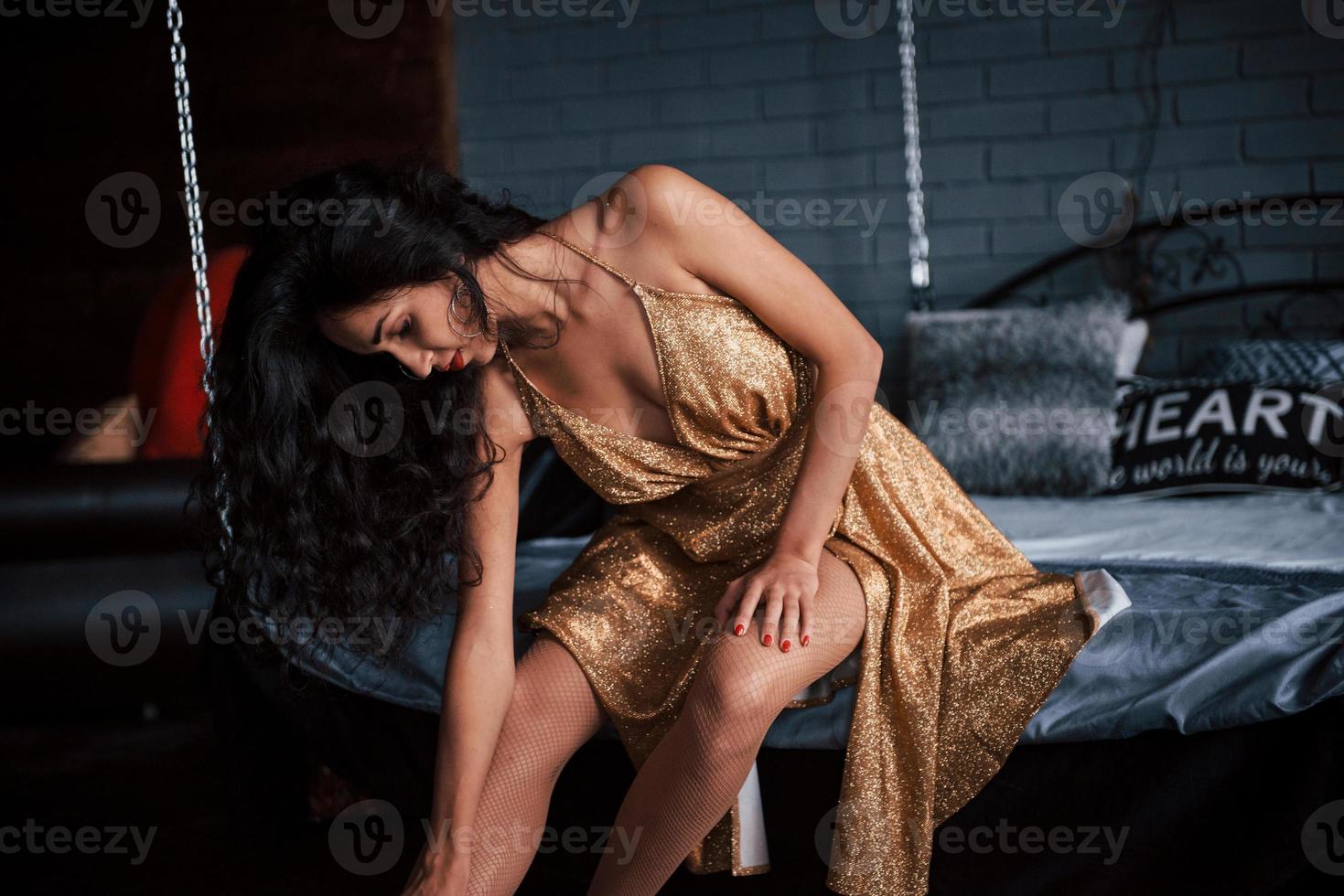 meisje in gouden jurk zit op wit bed aan de kettingen in luxe appartementen foto