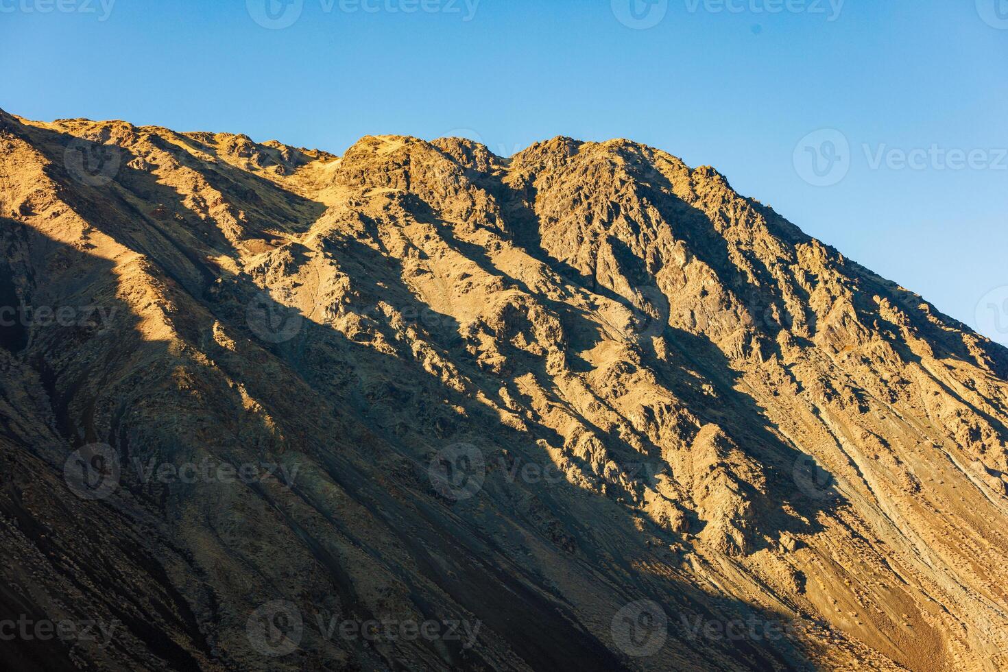 dichtbij omhoog visie van een berg kant onder direct avond zon licht met Doorzichtig blauw lucht bovenstaande. foto