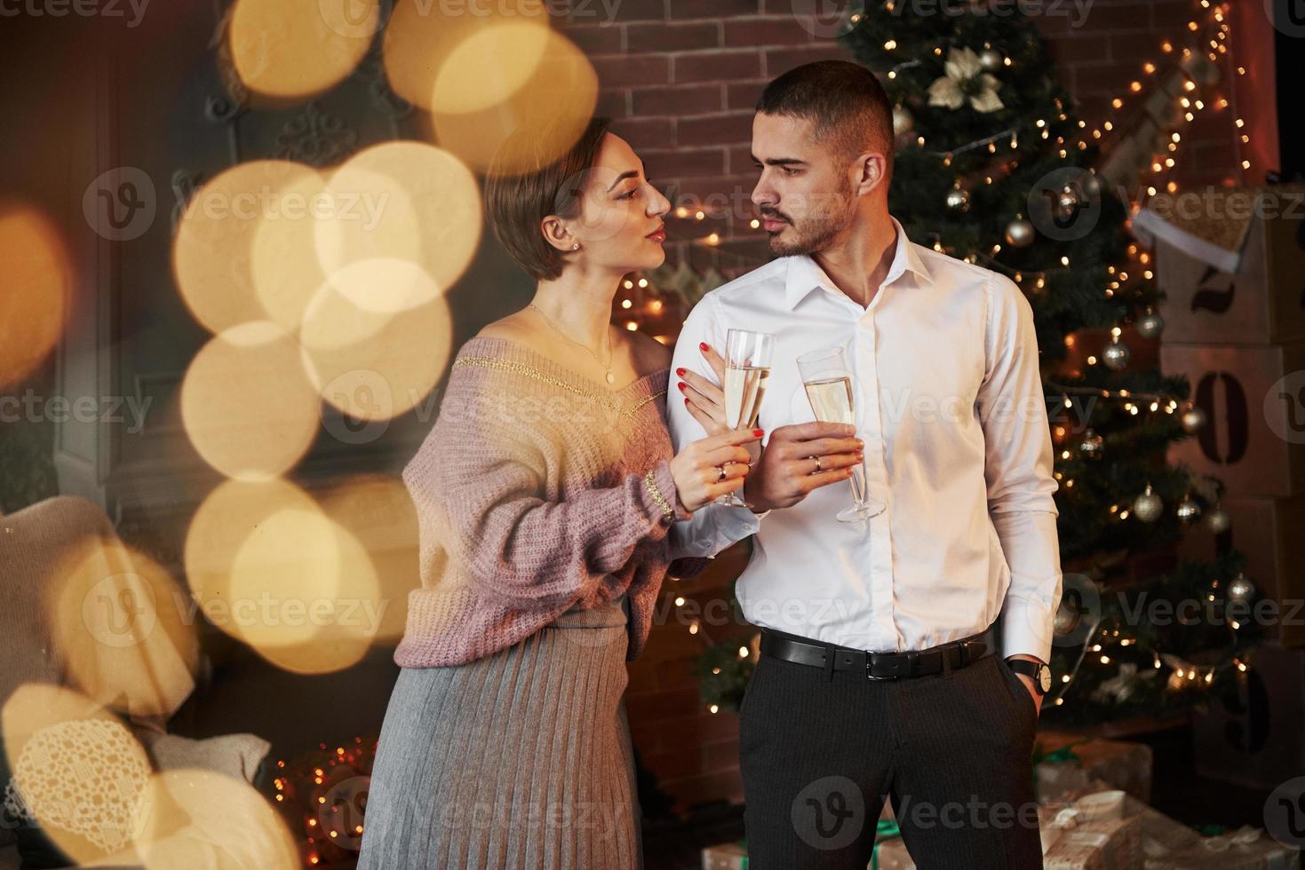 vrouw klampt zich vast aan haar man. leuk stel dat nieuwjaar viert voor de kerstboom foto