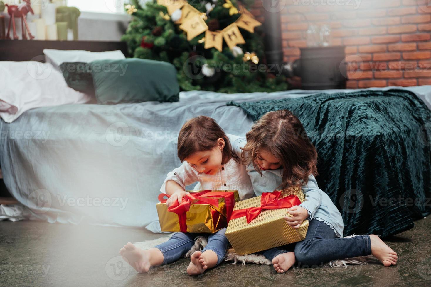 vrienden omhelzen elkaar. kerstvakantie met cadeaus voor deze twee kinderen die binnen zitten in de mooie kamer bij het bed foto